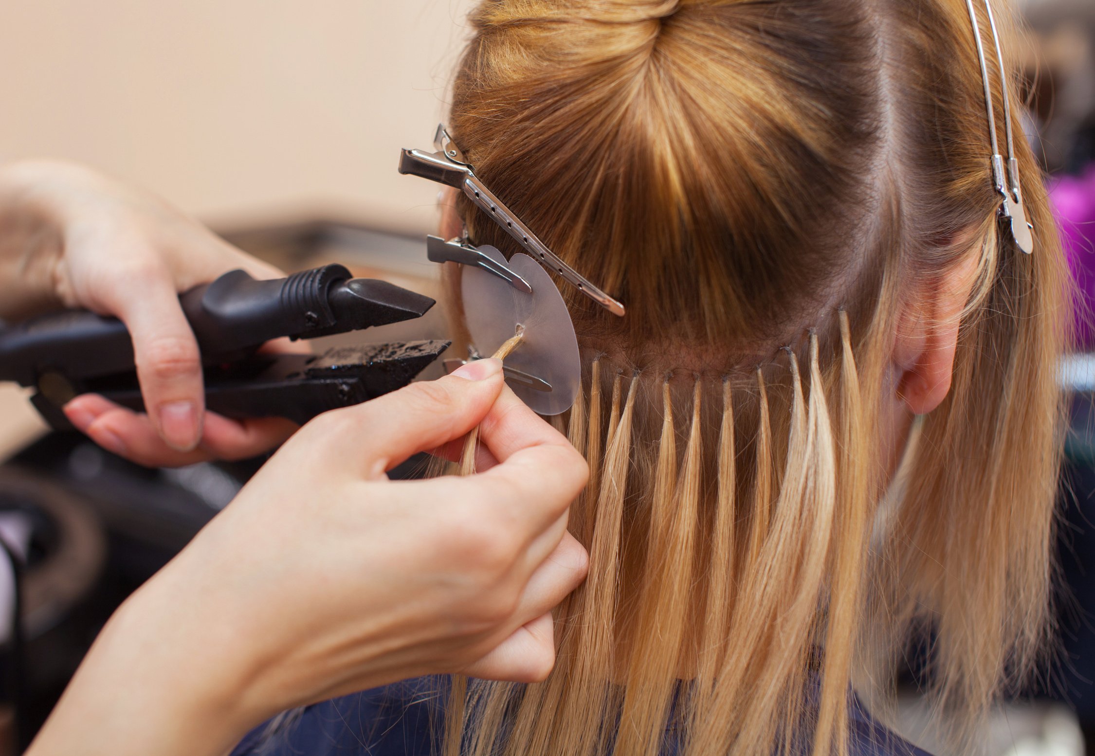 The hairdresser does hair extensions to a young girl, a blonde in a beauty salon.